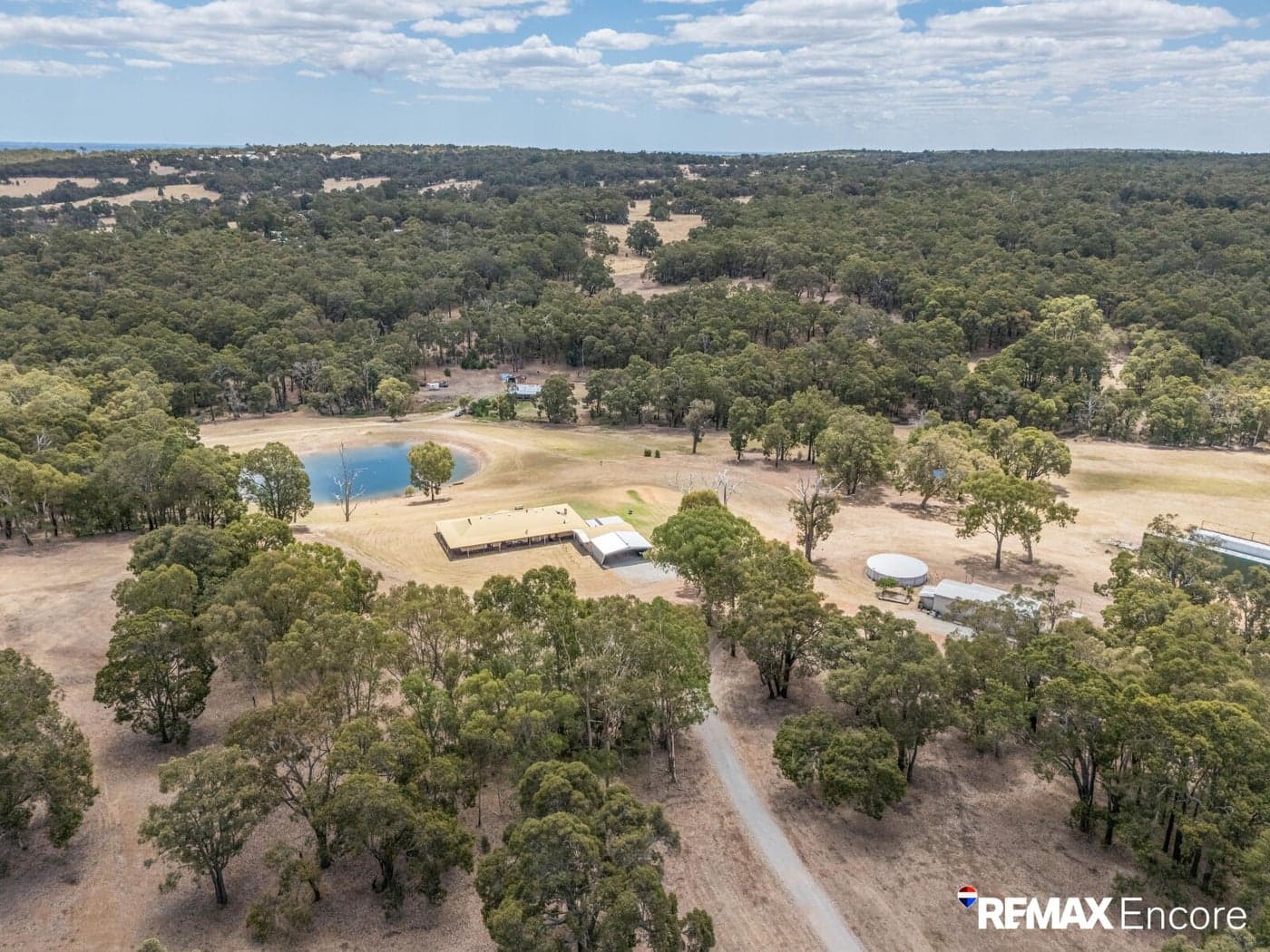 Aerial view of a rural house and pond nestled within an expansive green forest.