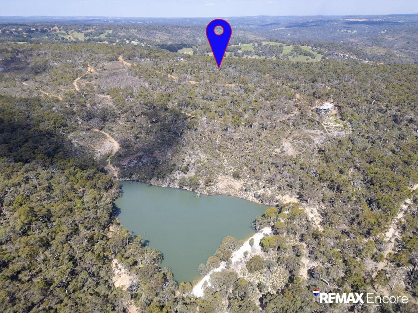 Aerial view of a lake surrounded by dense forest with a blue location pin.